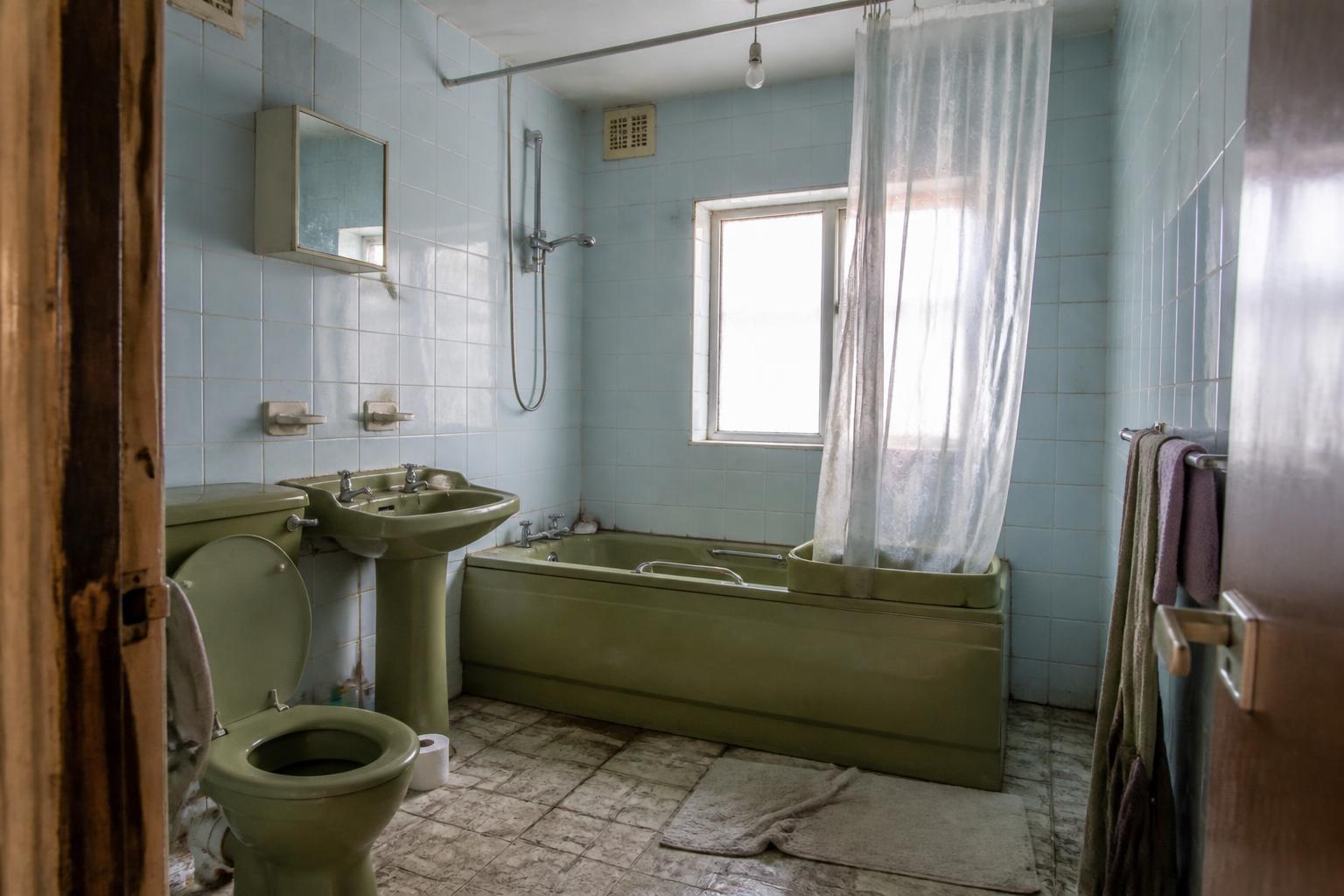 Study of a dated small bathroom before: cracked pale blue tiles, avocado suite, plastic shower curtain and a bare bulb