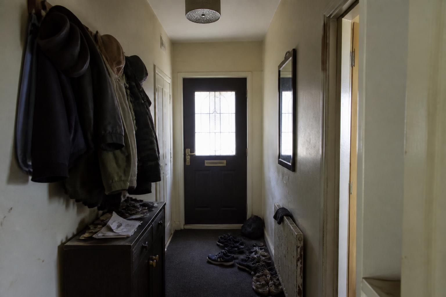 Study of a dark cluttered apartment hallway before: dingy walls, worn carpet, overloaded coat hooks and shoes on the floor
