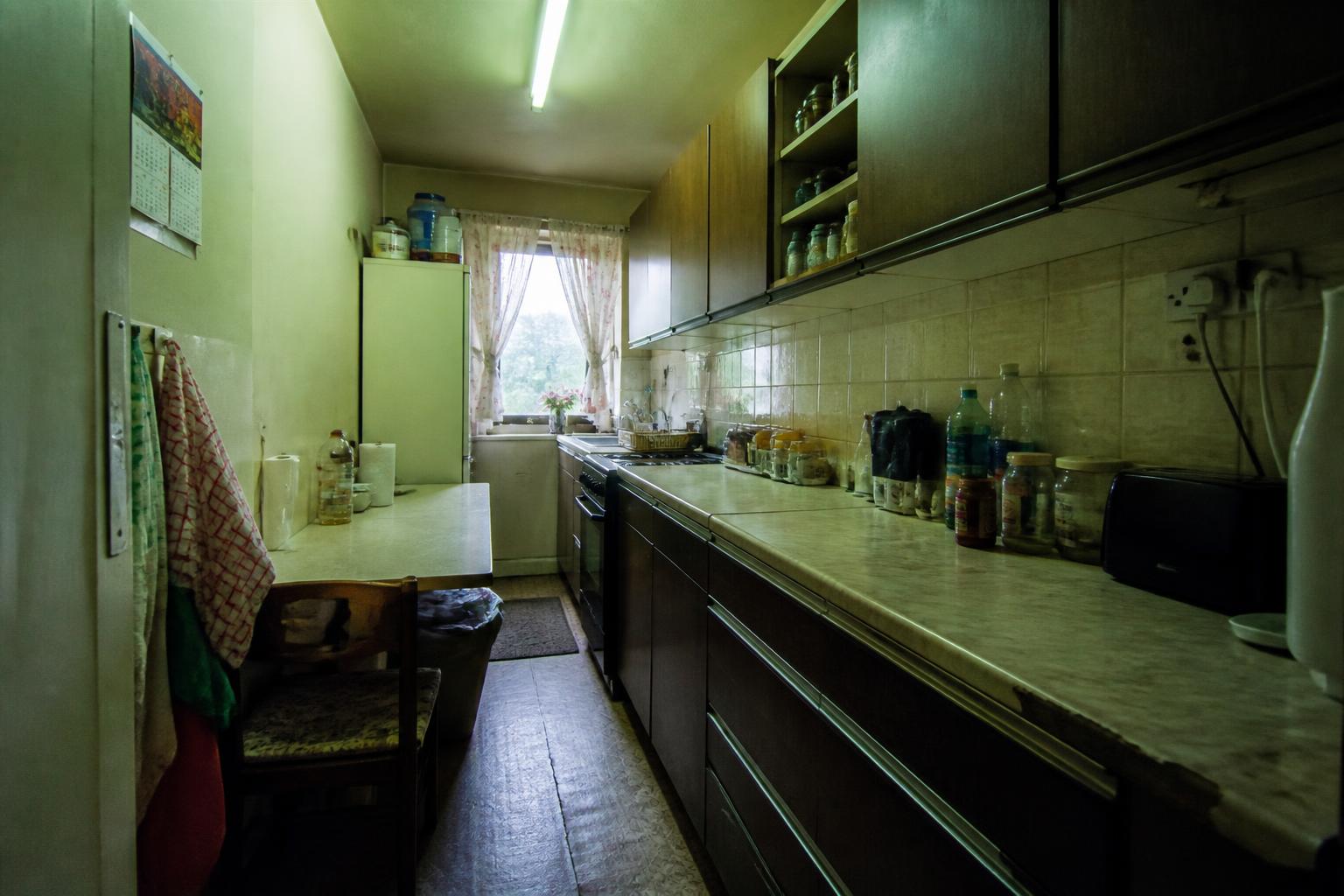 Study of a dated galley kitchen before: dark brown units, cluttered laminate worktop, fluorescent strip light and cracked vinyl floor